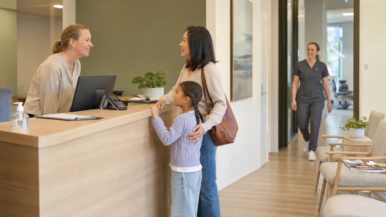 A parent and child being welcomed at a dental practice reception desk
